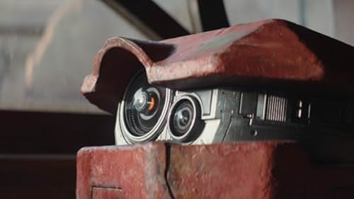 A closeup on a little red droid with a gray area with sensors and a camera that looks like a face.