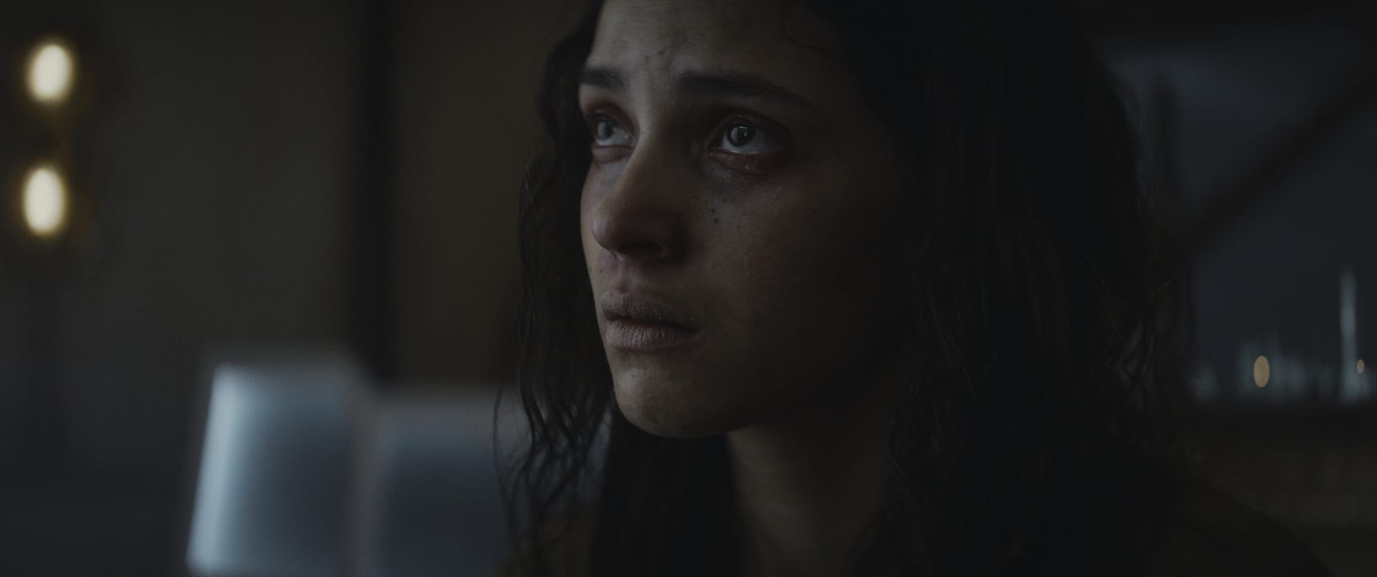 A young woman with disheveled hair looks beaten up and almost broken but still defiant after being tortured.