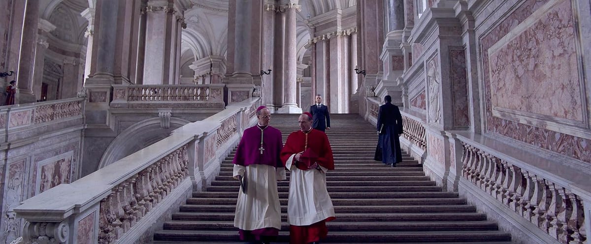 O'Malley (Bryan F. O'Byrne) and Lawrence (Ralph Fiennes) talk and walk down an opulent staircase in Conclave.