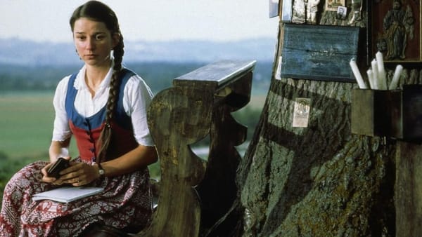 Sonja (Lena Stolze) sits on a bench in front of a tree covered in religious images and icons in The Nasty Girl 