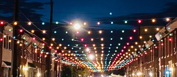 multi-colored strands of lights are strung across a city street, with houses on either side of the street.